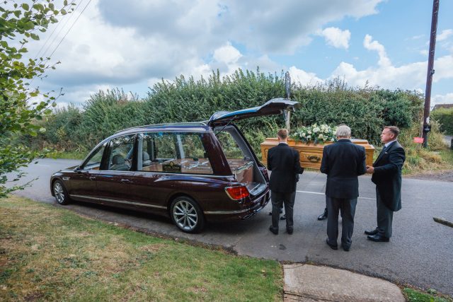 Alex Jones Funeral Directors - Coffin with floral spray being carried into a black hearse